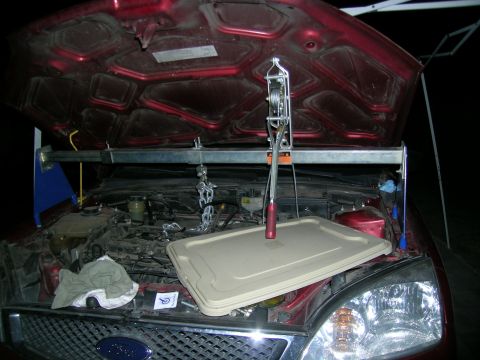 1995 Ford Probe - Engine hoist is positioned over the engine bay of a 1995 Ford Probe, with a plastic cover resting on the fender.
