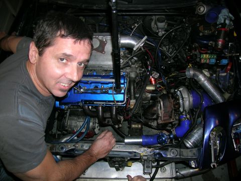 1995 Ford Probe - A man poses with a custom-built car engine a turbocharger and vibrant blue components.