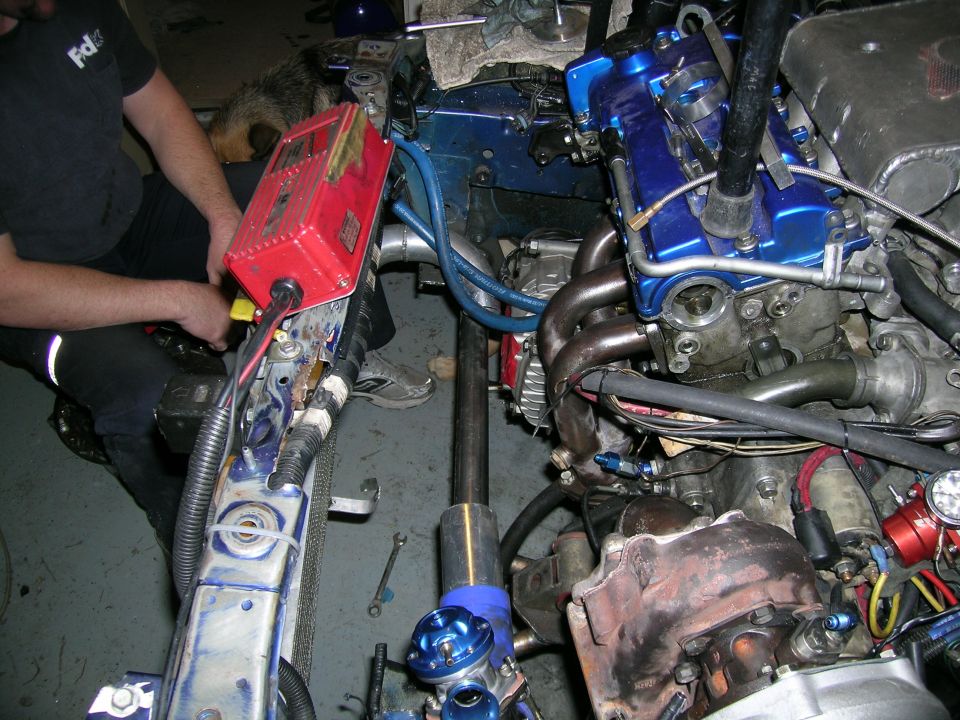 Close-up of a car engine bay with turbo parts, blue valve cover, and a red control box