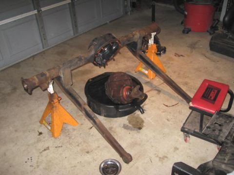 1963 Ford Galaxie - A disassembled rear axle assembly rests on jack stands in a garage, with the differential in a drain pan.