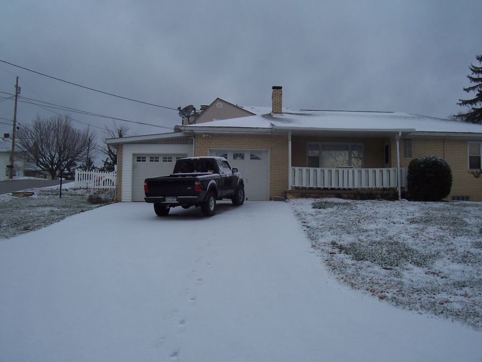 Black pickup truck in a snowy driveway in front of a house with a garage