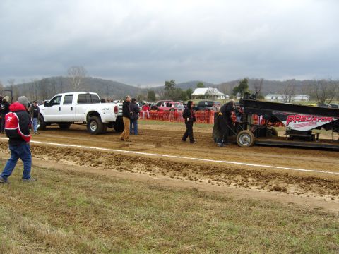 2007 Ford Mustang - A white pickup truck is positioned next to a sled at an outdoor event, with several people observing.