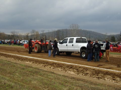 2007 Ford Mustang - A white pickup truck and an orange tractor are positioned on a dirt track during an event.