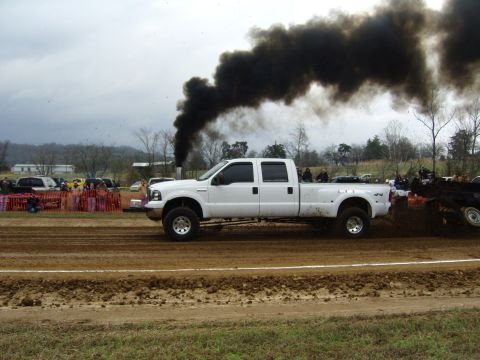 2007 Ford Mustang - A white pickup truck pulls a sled, emitting a large plume of black smoke during a pull event.