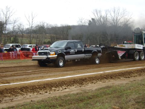 2007 Ford Mustang - A black Ford F-250 Super Duty truck competes in a pull event, kicking up dirt as it moves forward.