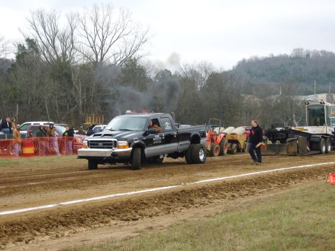 2007 Ford Mustang - A black Ford F-350 Super Duty pickup truck competes in a pull event, kicking up dust and smoke.