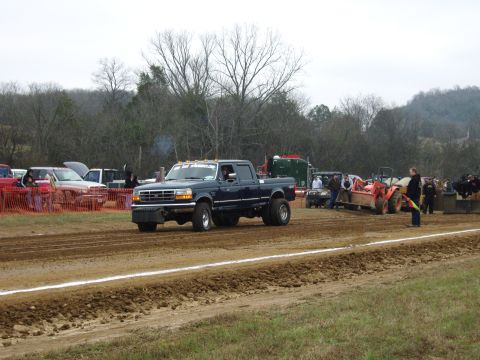 2007 Ford Mustang - A dark blue pickup truck competes in a pull event, with spectators and other vehicles in the background.