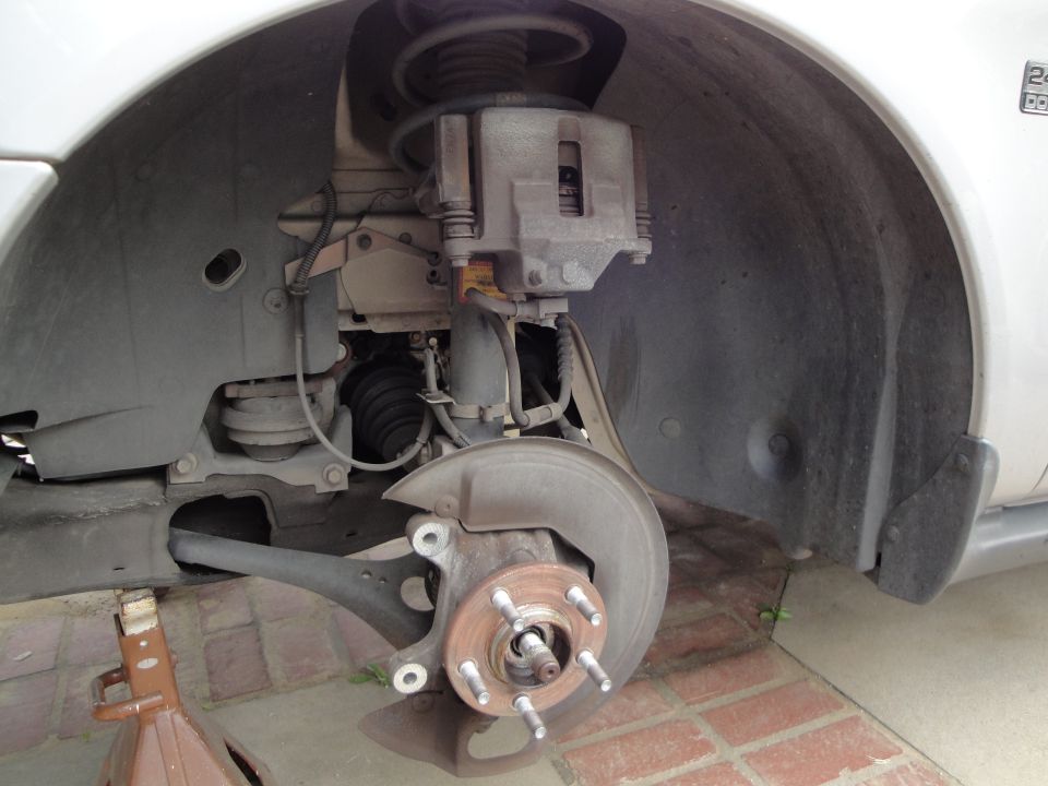 Front suspension and brake assembly with wheel removed on white car: caliper, rotor, strut, CV boot