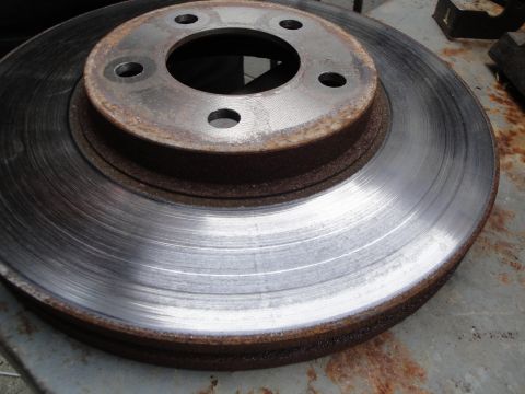 2003 Ford Taurus - A worn and rusted brake rotor sits on a metal surface, showing signs of age and use.
