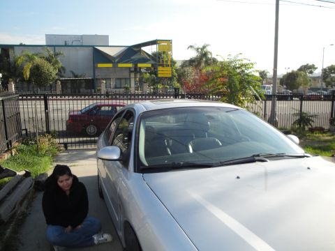 2003 Ford Taurus - A silver sedan is parked in a driveway with a woman sitting beside it.