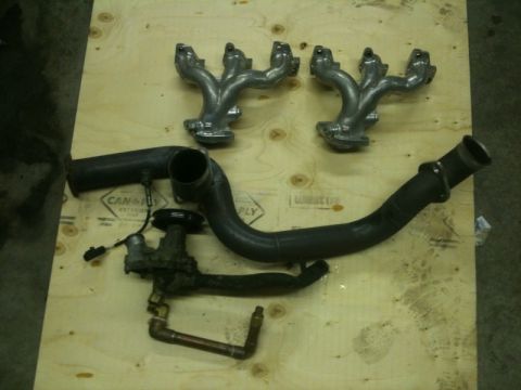 1990 Ford Probe - A collection of exhaust system components and a water pump are laid out on a wooden surface.