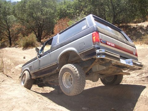 1989 Ford Bronco - 1989 Ford Bronco navigating an off-road trail with steep inclines and loose dirt.