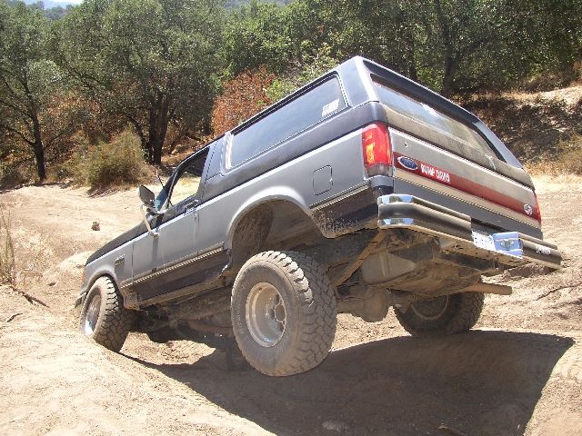 Gray Ford Bronco SUV flexing over a dirt mound on an off-road trail, rear view