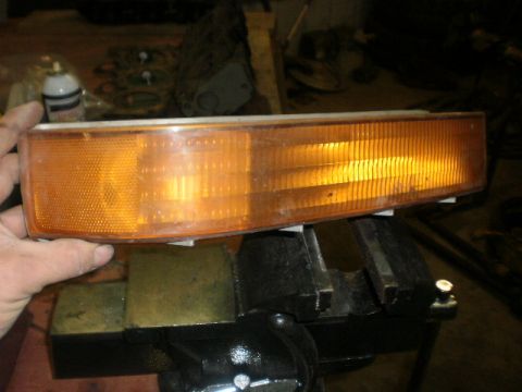 1995 Ford Bronco - An amber turn signal assembly is held in a vise, ready for installation or repair.