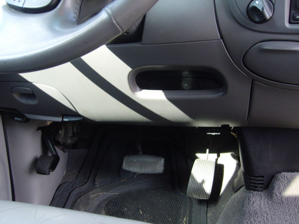 Vehicle interior showing steering column, pedals, and dashboard trim with diagonal stripes