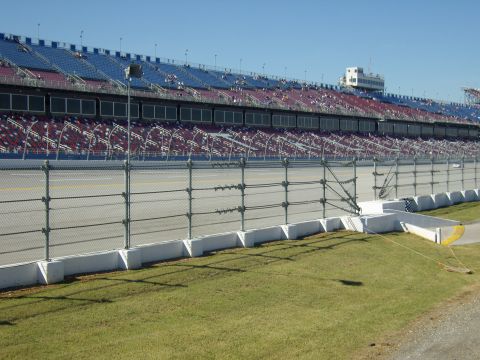 2007 Ford Mustang - A view of a racetrack and its grandstands under a clear blue sky, with a chain-link fence in the foreground.