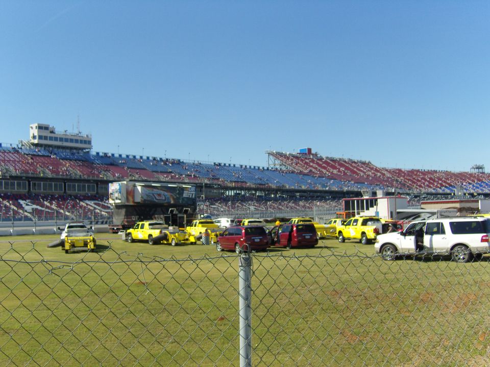 Yellow trucks and red vans parked at a racetrack grandstand