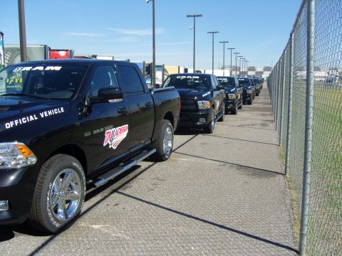 2007 Ford Mustang - A line of black Ram 1500 pickup trucks are parked next to a chain-link fence under a clear blue sky.
