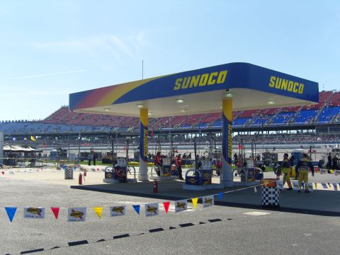 2007 Ford Mustang - Sunoco gas station canopy with colorful stripes, race track grandstands in background, sunny day.