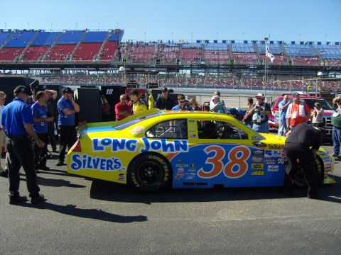 2007 Ford Mustang - A race car with sponsor decals is being serviced by a crew in front of a grandstand filled with spectators.