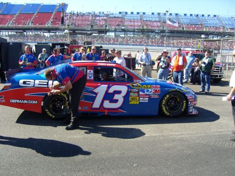 2007 Ford Mustang - A race car with multiple sponsor decals is being serviced by a crew member in a pit lane.