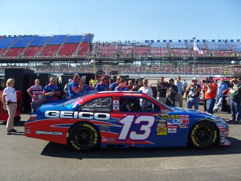 2007 Ford Mustang - A race car with GEICO sponsorship and the number 13 is parked on the track with spectators in the background.