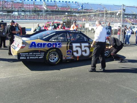 2007 Ford Mustang - A race car with sponsor decals is being serviced by a pit crew member during a race event.