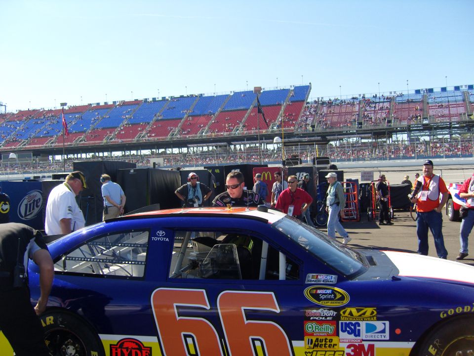 NASCAR race car with number 66, pit crew and spectators in background