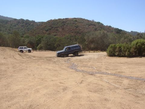 1989 Ford Bronco - A dark blue 1989 Ford Bronco navigates a dusty off-road course alongside another white SUV.