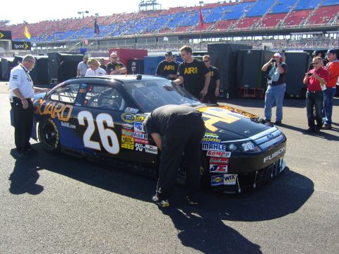 2007 Ford Mustang - A black race car with prominent sponsorship decals and the number 26 is being attended to by crew members at a race track.