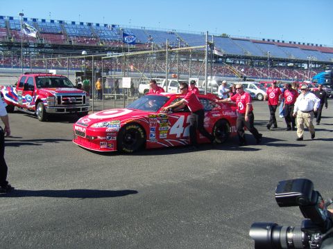 2007 Ford Mustang - Race car crew pushes a car on the track with a support truck visible.