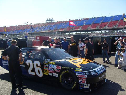 2007 Ford Mustang - A black and yellow race car, identified as a Ford Fusion, is parked on a track with a crowd of people around it.