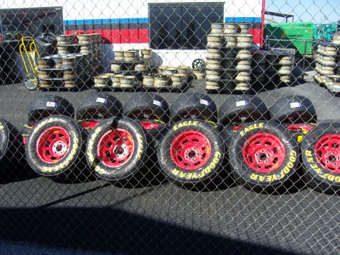 2007 Ford Mustang - A row of race car tires with red wheels and prominent Goodyear Eagle branding are lined up behind a chain-link fence.
