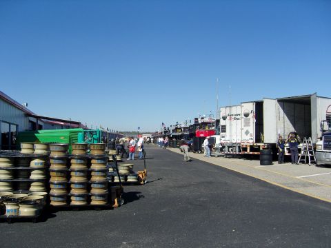 2007 Ford Mustang - Semi-trucks and stacked tires are visible on a sunny day at a race track pit lane.