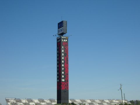 2007 Ford Mustang - A tall scoreboard tower displays lap times at a racetrack, with grandstands in the background under a clear blue sky.