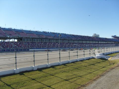 2007 Ford Mustang - Multiple race cars are visible on a track with spectators in the grandstands.