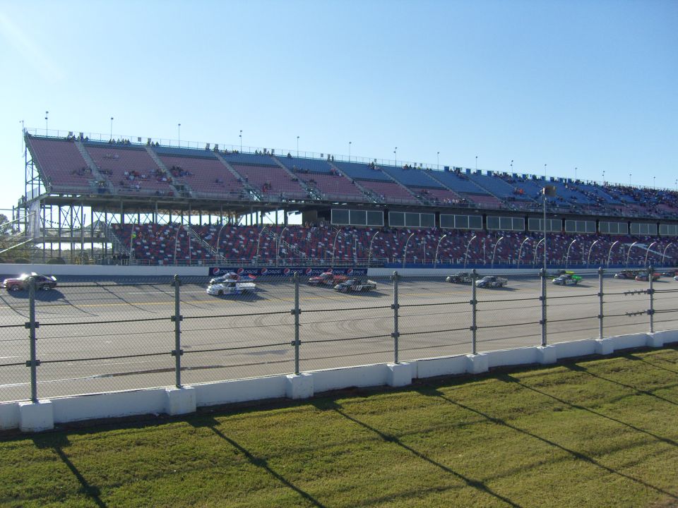 Stock cars racing on a track in front of a large grandstand filled with spectators