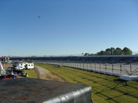 2007 Ford Mustang - Multiple race cars are on a track, with spectators and RVs visible in the background.