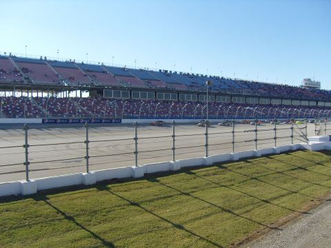 2007 Ford Mustang - Multiple race cars are visible on a track in front of a large grandstand filled with spectators.