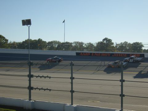 2007 Ford Mustang - Multiple stock cars compete on a race track under a clear sky.