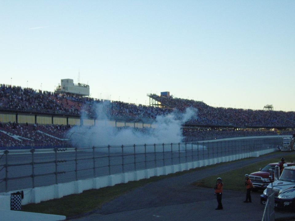 Race track with smoke billowing from the track and a large crowd in the stands