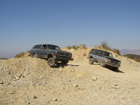 1989 Ford Bronco - Two SUVs navigate a challenging off-road terrain on a sunny day.