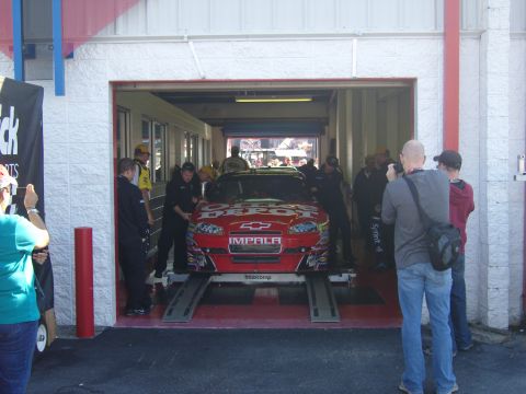 2007 Ford Mustang - A red race car with "DEPOT" and "IMPALA" text is positioned on a lift inside a garage bay.