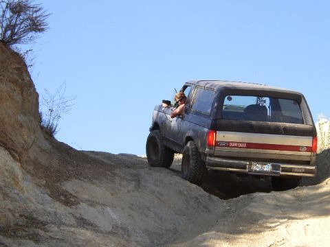 1989 Ford Bronco - 1989 Ford Bronco navigating a challenging off-road trail on a sunny day.