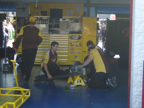 2007 Ford Mustang - Pit crew members are seen working on a car's suspension system in a garage setting.