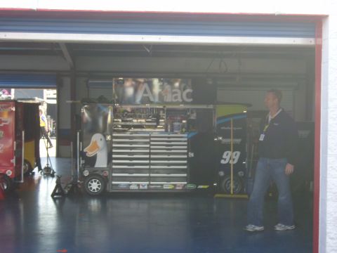 2007 Ford Mustang - A pit garage scene with tool chests and a race car numbered 99 is visible, along with a man standing nearby.