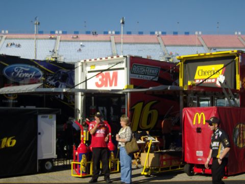 2007 Ford Mustang - Race day scene with multiple sponsor-branded trailers and spectators in the background.