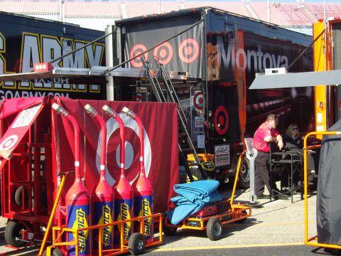 2007 Ford Mustang - Pit lane scene with large racing trailers, fuel cans, and crew members.