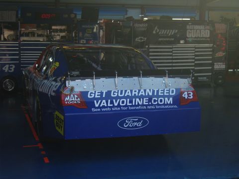 2007 Ford Mustang - A race car with sponsor decals is parked in a garage bay.