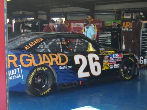 2007 Ford Mustang - Side view of race car #26 in a garage, showing sponsor decals and "ALABAMA" on the roof.